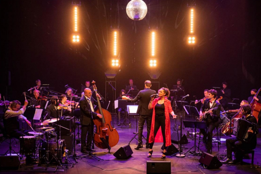 Sur une scène colorée, l'orchestre entoure la chanteuse qui est habillée en rouge vif. Au dessus d'eux se trouve une boule disco.
