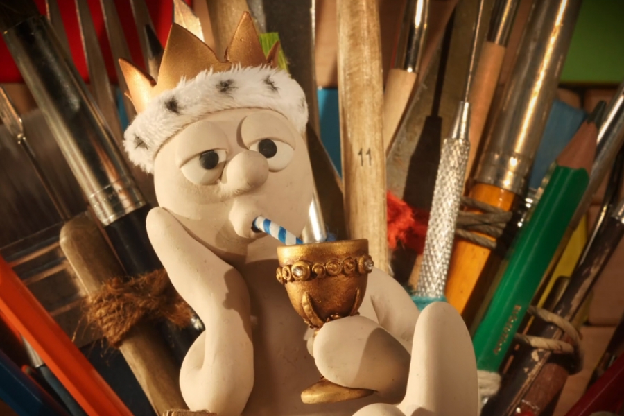 Coiffé d'une couronne dorée, Morph est sur un trône en crayons de papier et sirote une boisson dans une coupe en or.