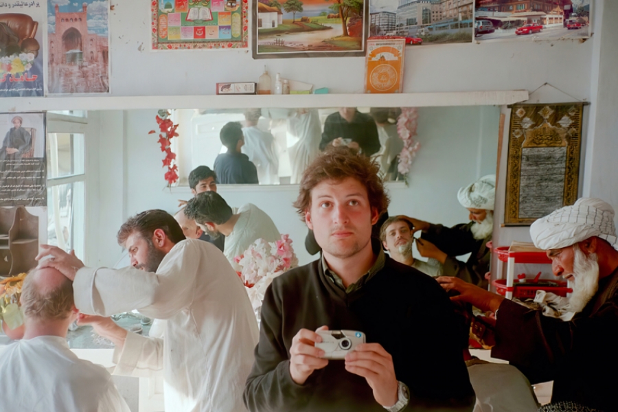 Claude Baechtold se prend en photo dans le miroir d'un barber. Derrière lui, des hommes se font couper la barbe. 
