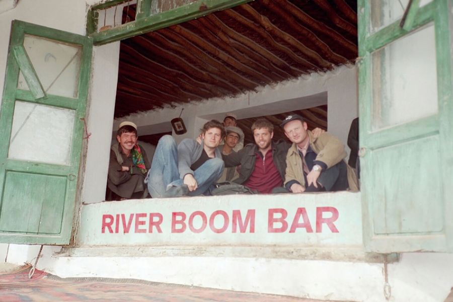 Des hommes sont postés dans l'encadré d'une grande fenêtre à battants, où il est écrit en rouge "River boom bar" 