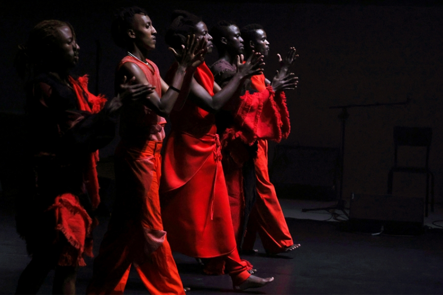 Sur scène, des interprètes vêtues de robes rouges sont en ligne.