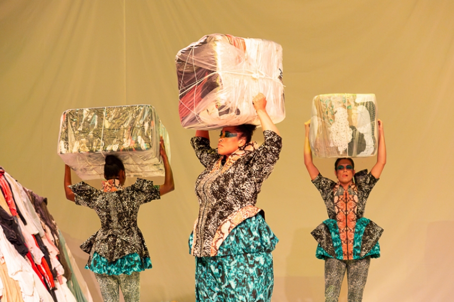 Trois femmes portent des cubes de vêtements sur leurs têtes.