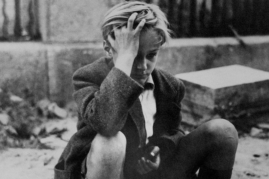 Photo en noir et blanc. Gros plan sur le jeune garçon qui est assis et semble inquiet. Il regarde dans le vide, la main sur sa tête, les cheveux ébouriffé.