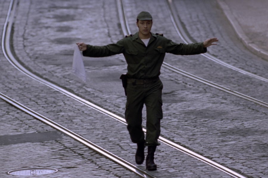 Au milieu de la rue qui est déserte, un soldat marche les bras en l'air, en tenant un mouchoir blanc, comme symbol de paix.