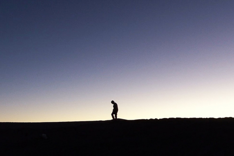 Dans le désert, une personne marche en regardant le sol. Le ciel est dégagé.
