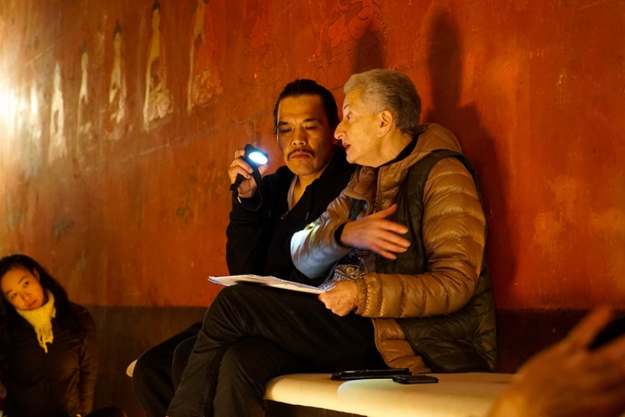 Assis contre un mur rouge, un homme et Hélène Cixous lisent des feuilles et discutent ensemble.