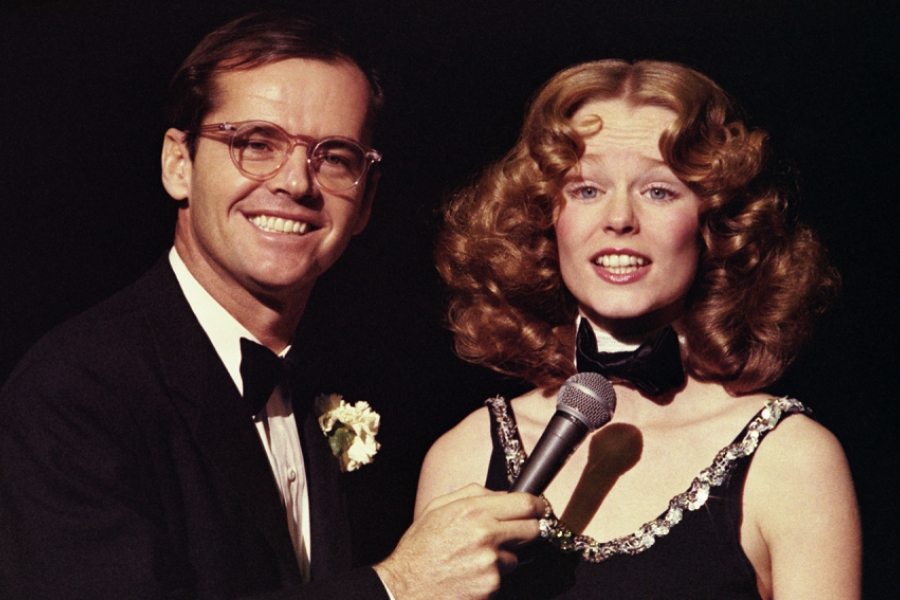 Sur scène, Jack Nicholson sourit et tend le micro à une femme.