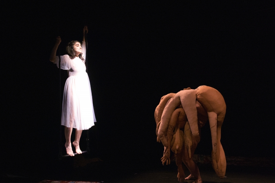 Une comédienne sous la lumière, sur une balançoire, face à une sorte de monstre/marionnettes