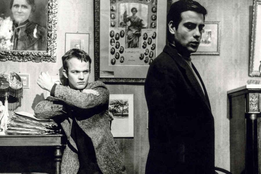 Noir et blanc. Le frère est assis à table et semble contrarié. Il a le poing serré.