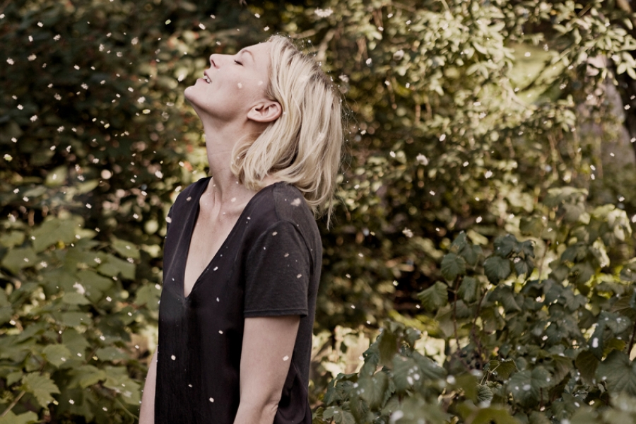 Une femme blonde est dans un jardin où il y a des petites particules dans l'air 