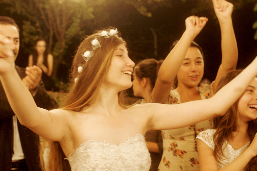 Gros plan sur une jeune fille qui danse les bras en l'air et qui porte une couronne de fleurs. Elle est entourée de ses soeurs.