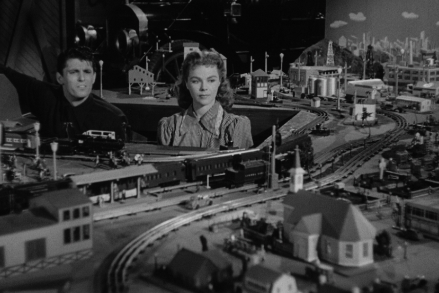 Un homme et une femme regardent attentivement la maquette d'un train qui prend toute la place.