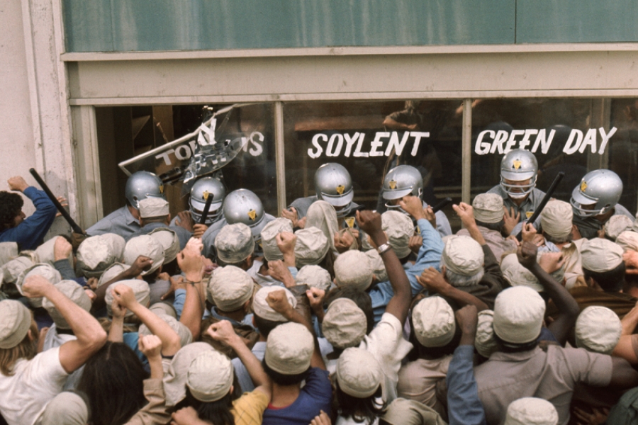 Une foule de personne dans le besoin est en colère devant une devanture protégée par des forces de l'ordre