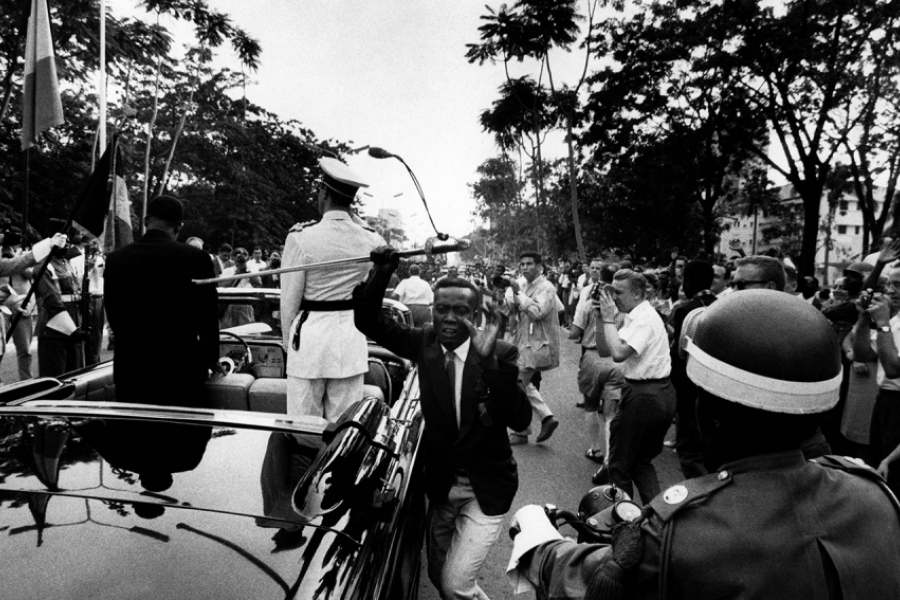 Dans la rue, des gens sont agglutinés pour prendre en photo une voiture avec des personnes 