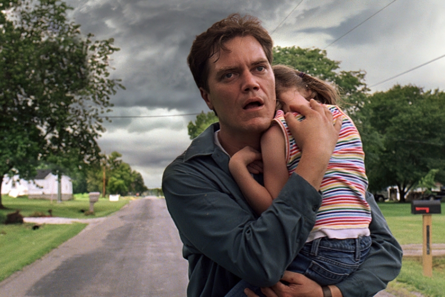 Au milieu d'une route, un homme tient sa petite fille dans ses bras pour la protéger d'une tempete qui arrive.