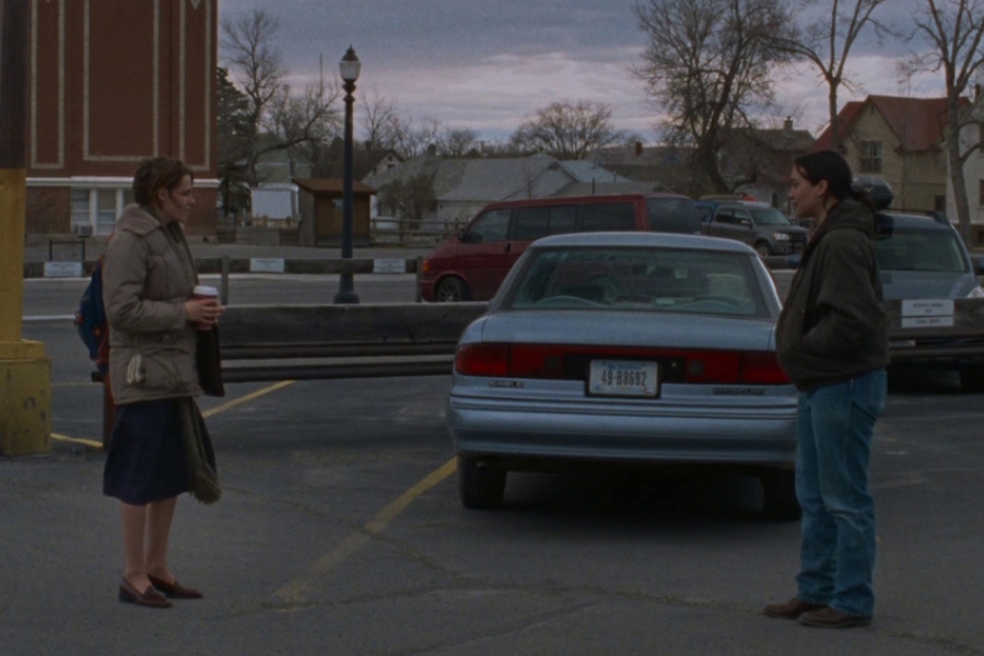 Sur un parking, devant une voiture garée, deux femmes se font face et se parlent, à quelques mètres l'une de l'autre