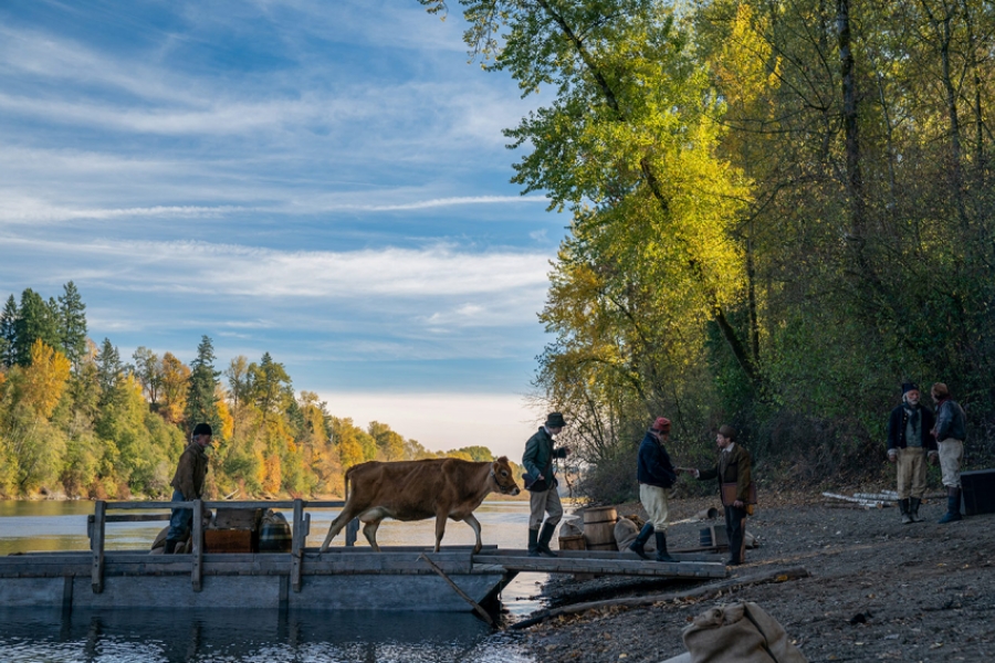 Ds hommes font traversée une vache sur un petit pont en bois au dessus d'un lac.
