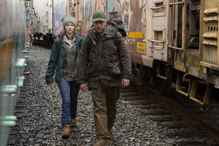 Un père et sa fille marchent entre deux trains tagués à l'arret.