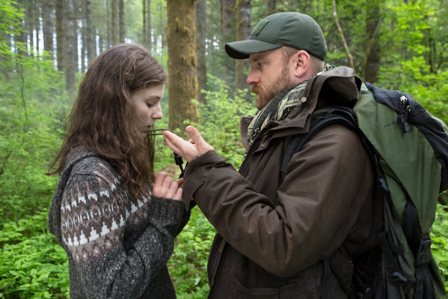 Dans une forêt, un père et sa fille se font face. Lui porte une casquette et un sac à dos. Il montre avec sa main le collier de la fille.