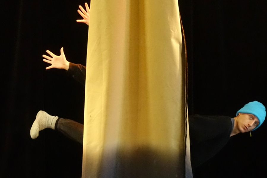 Un danseur est à l'horizontal derrière un tissus jaune qui descend du plafond 