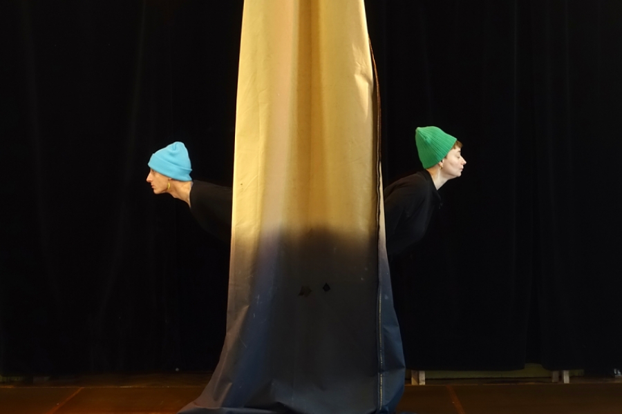 Deux danseurs sont dods à dos derrière un tissus jaune qui descend du plafond 
