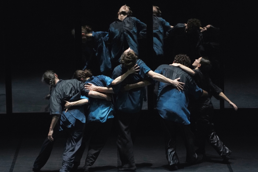 5 danseurs et danseuses, dos au public, se tiennent par les bras, leur image se reflétant dans un miroir 