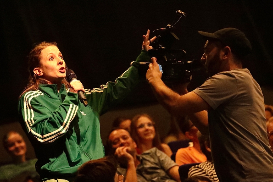 Une jeune femme prend la parole dans un micro tout en étant filmée par un cameraman 