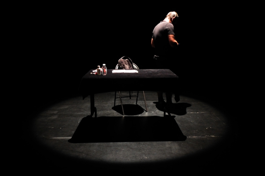 Interprète sur scène, avec juste une table noire