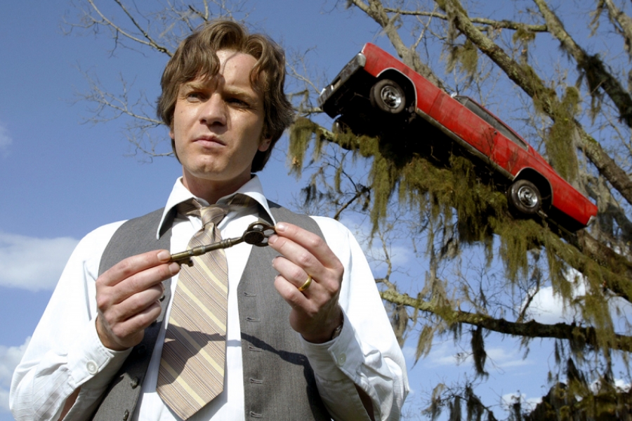 Un homme avec une clef, derrière lui, une voiture dans un arbre
